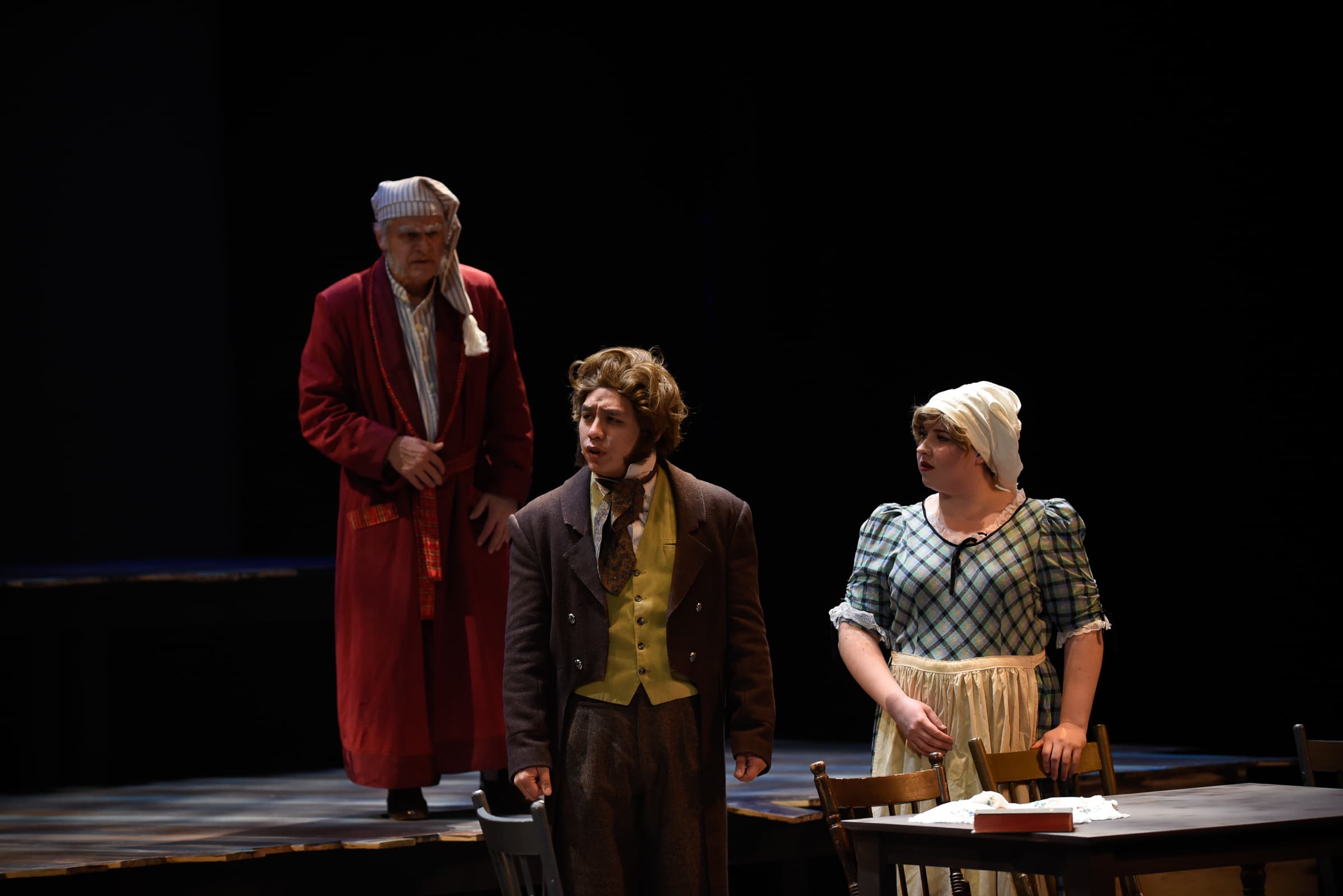 A scene from A Christmas Carol, where Scrooge is standing in his pyjamas and looking upon two other people.