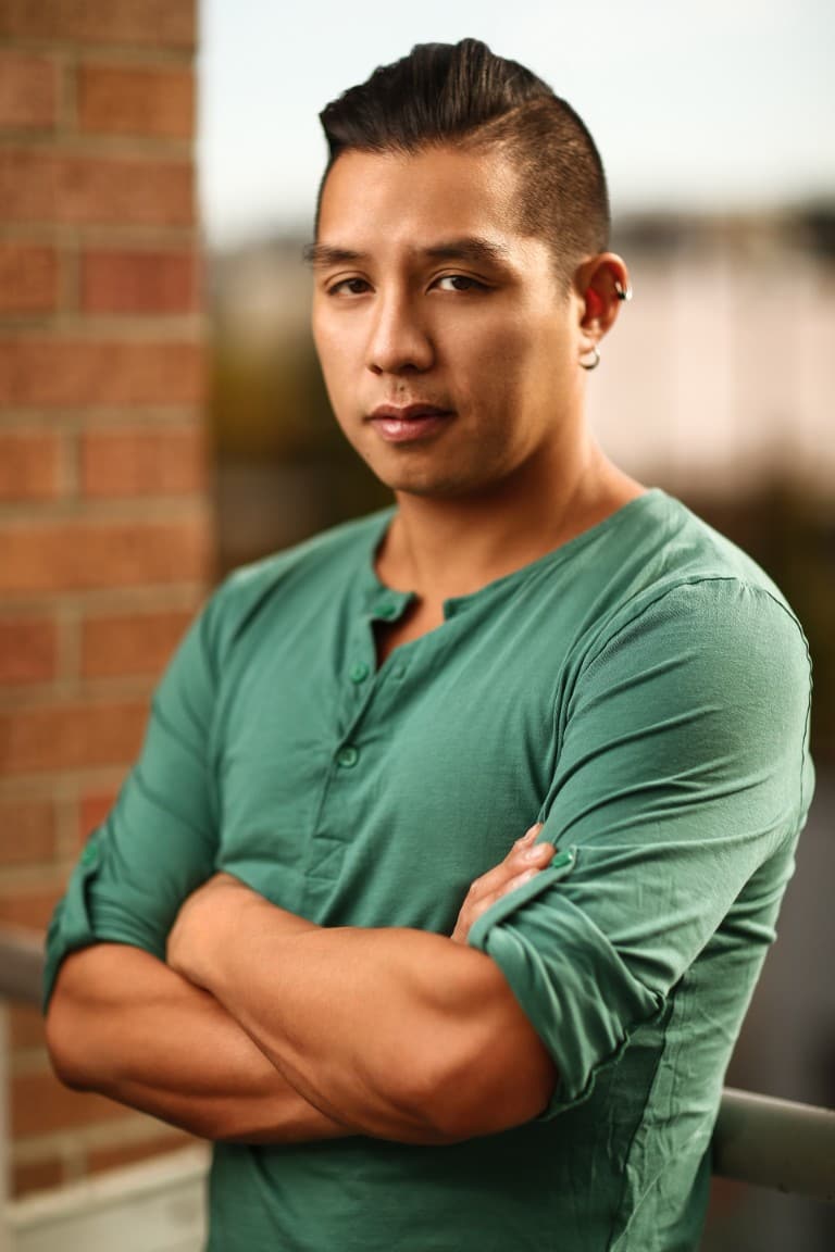 Aerhyn standing with his arms crossed and his body tilted to the side. He is looking intently into the camera.